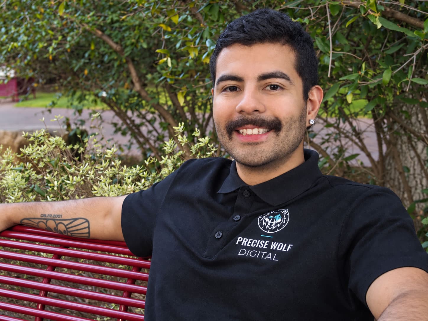 Ted Martinez, founder of Precise Wolf Digital, sitting on a park bench in a Precise Wolf Digital polo